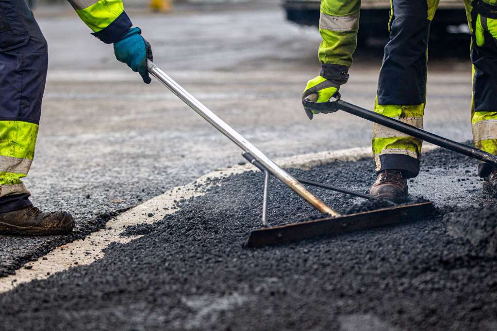 Kaksi työntekijää levittävät asfalttia.