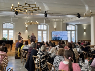 Teatteriravintolan Kulma täynnä ihmisiä sekä lavalla teatterinjohjaja ja ohjaaja.