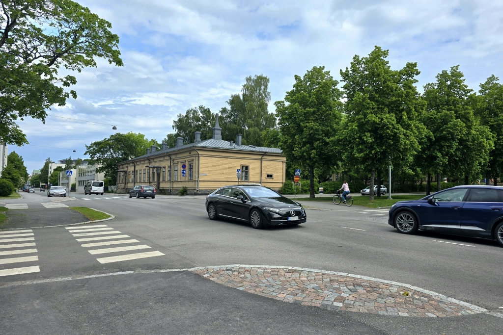 Katunäkymä, jossa autoja ajaa risteyksen läpi ja taustalla on vaalea, vanha rakennus.