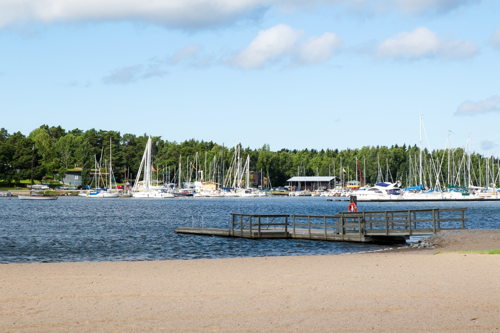 Beach, pier, and in the background a harbor with sailboats.