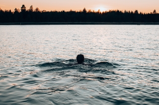 Henkilö uimassa auringonlaskun aikaan.