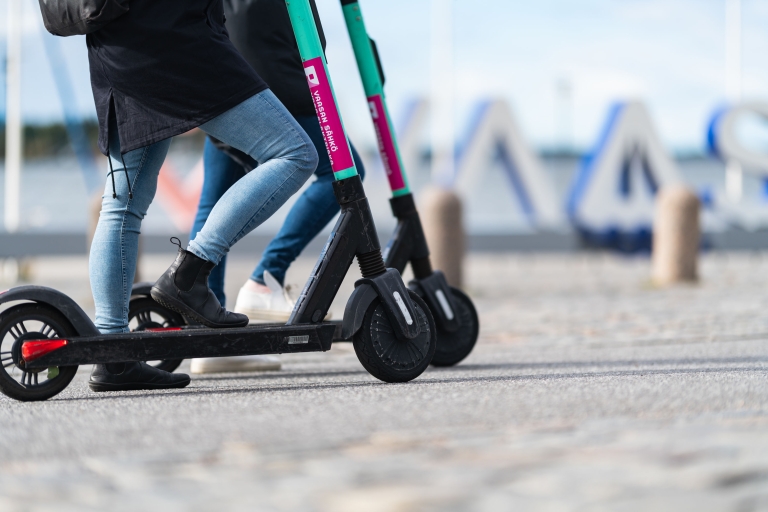 Kaksi henkilöä ajamassa sähköpotkulaudoilla mukulakivikadulla.