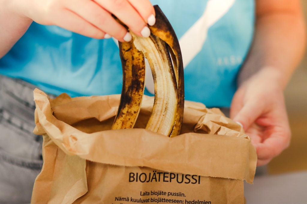 Henkilö laittaa banaaninkuoria paperiseen biojätepussiin.