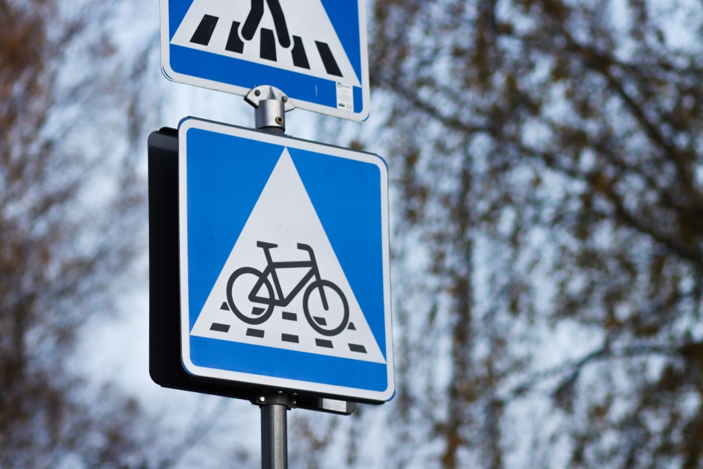 Vägmärke för cykelbana med blå bakgrund och ett vitt triangelformat fält med en cykelsymbol. I bakgrunden ett dimmigt landskap.