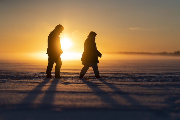 Two persons walking on the frozen sea during sunset.