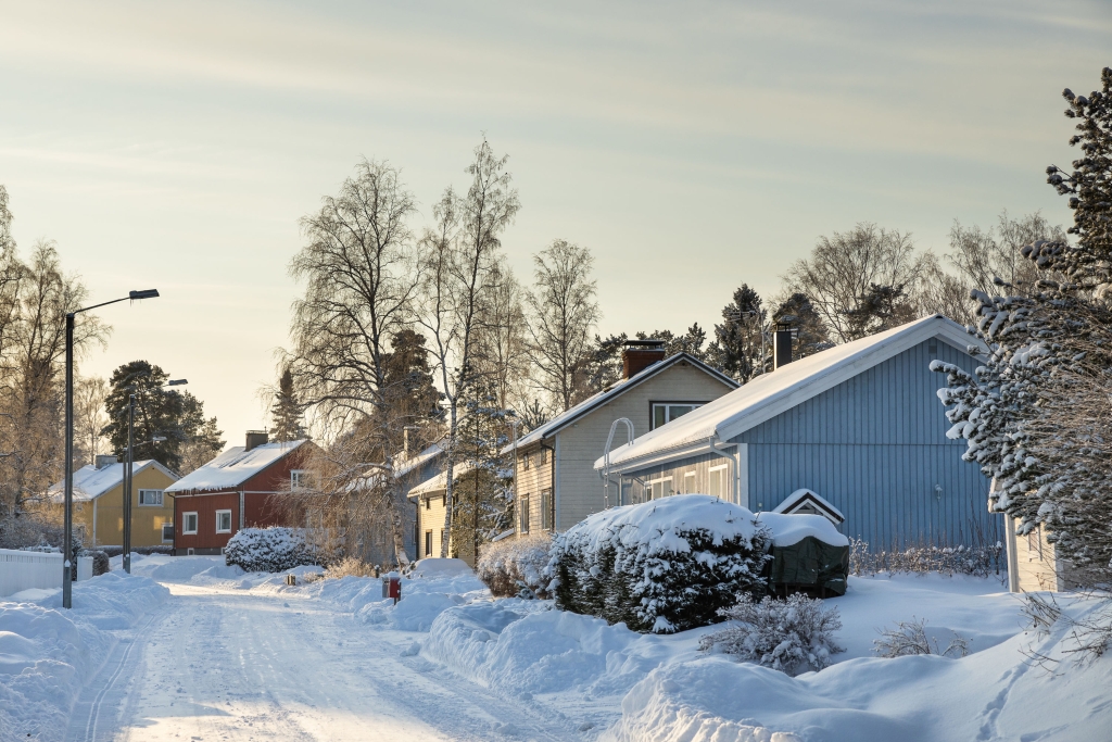 En snötäckt gata med enfamiljshus i olika färger i ett vinterlandskap.