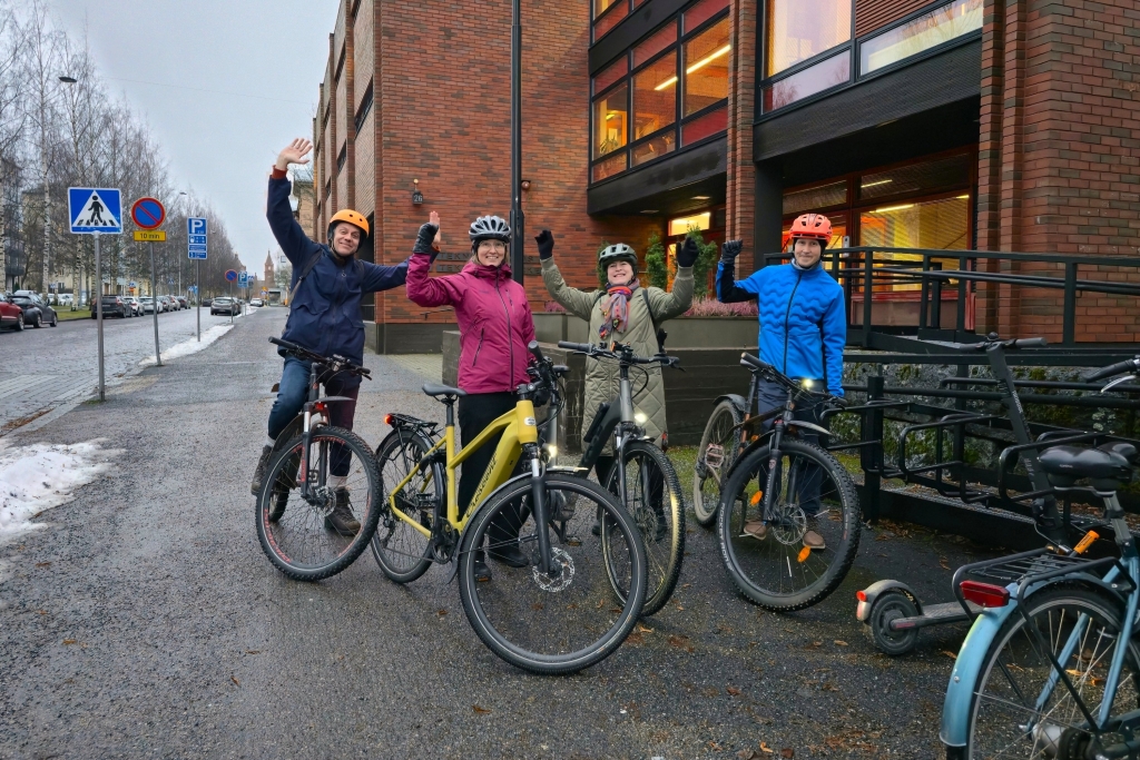 Neljä ihmistä seisoo polkupyörien kanssa tien reunalla talvisessa ympäristössä.