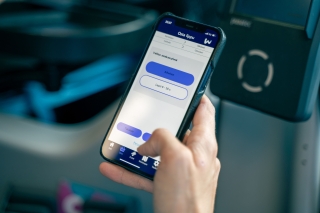Käsi pitää älypuhelinta joukkoliikennevälineen istuimella; puhelimen näytöllä on lipun ostonäkymä, jossa valitaan asiakasryhmä (aikuinen tai lapsi).