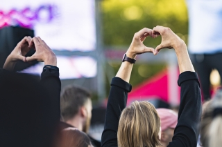 Kaksi ihmistä festivaalien yleisössä. Näyttävät käsillään sydämiä lavalle päin.