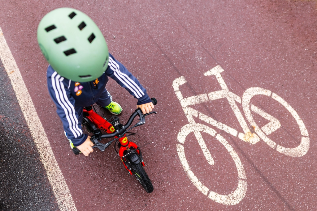 Lapsi ajaa punaisella polkupyörällä pyörätien merkinnän vieressä.