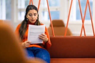 A woman is sitting and readin a paperdocument.