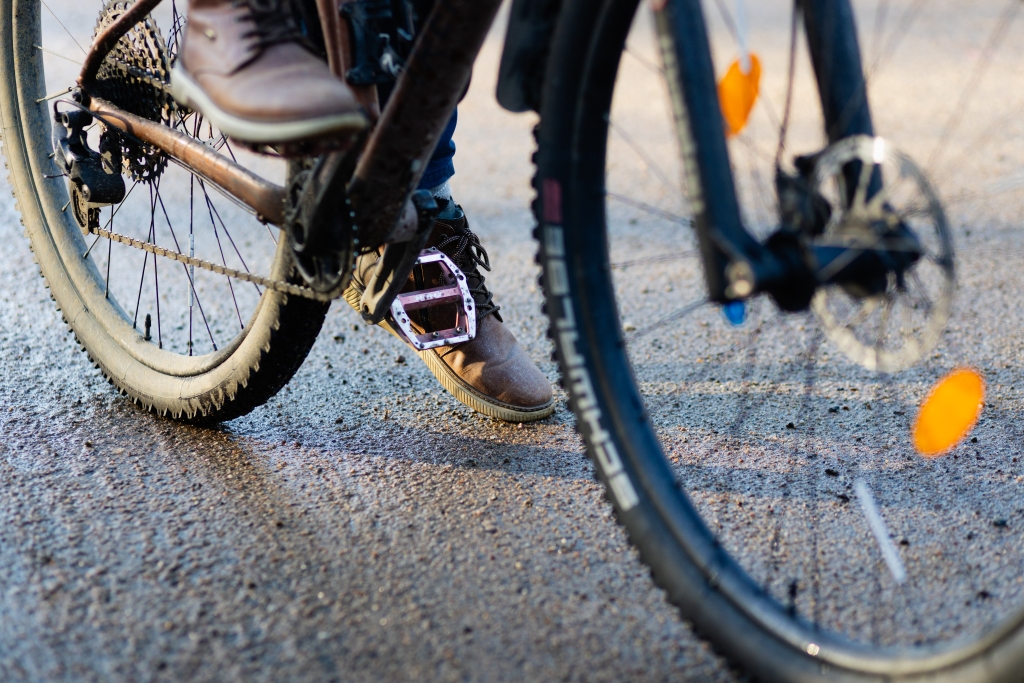 Lähikuva pyöräilijän jaloista ja pyörän renkaista polkemassa pyörätiellä, jonka päällä on hiekoitushiekkaa.