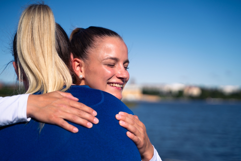 Kaksi naista haalavat. Toinen naisista hymylee. Taustalla merimaisema.