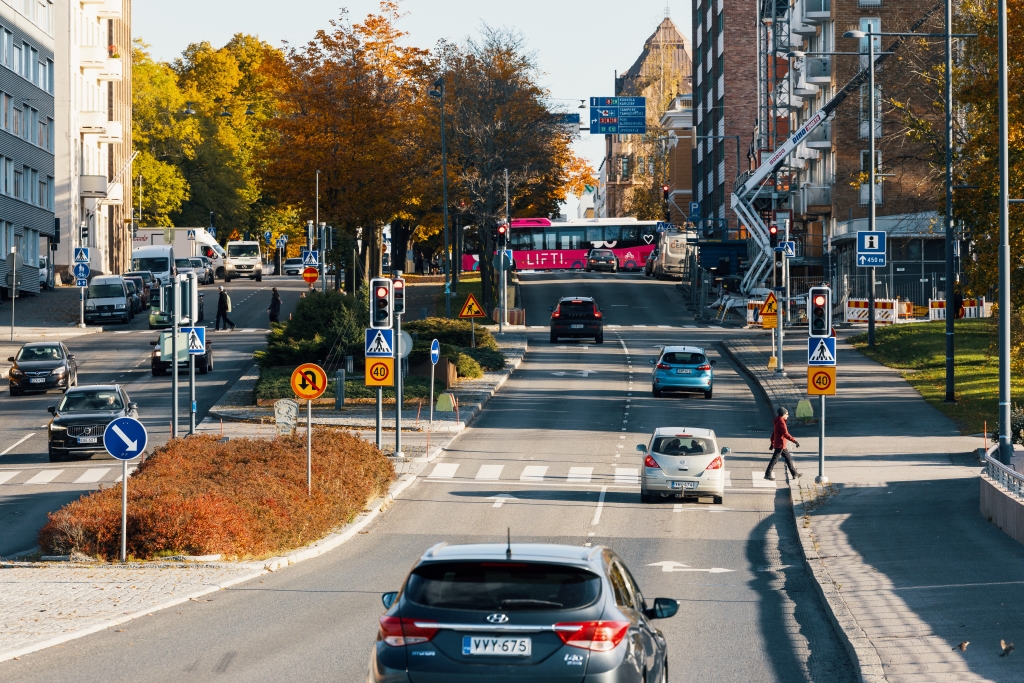 Autoja, kävelijöitä ja linja-auto puistikolla