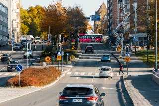 Autoja, kävelijöitä ja linja-auto puistikolla