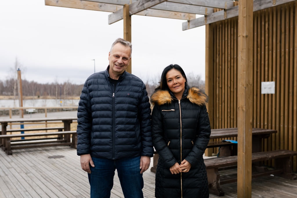 Två personer står utomhus på en träterrass på stranden i vinterjackor.