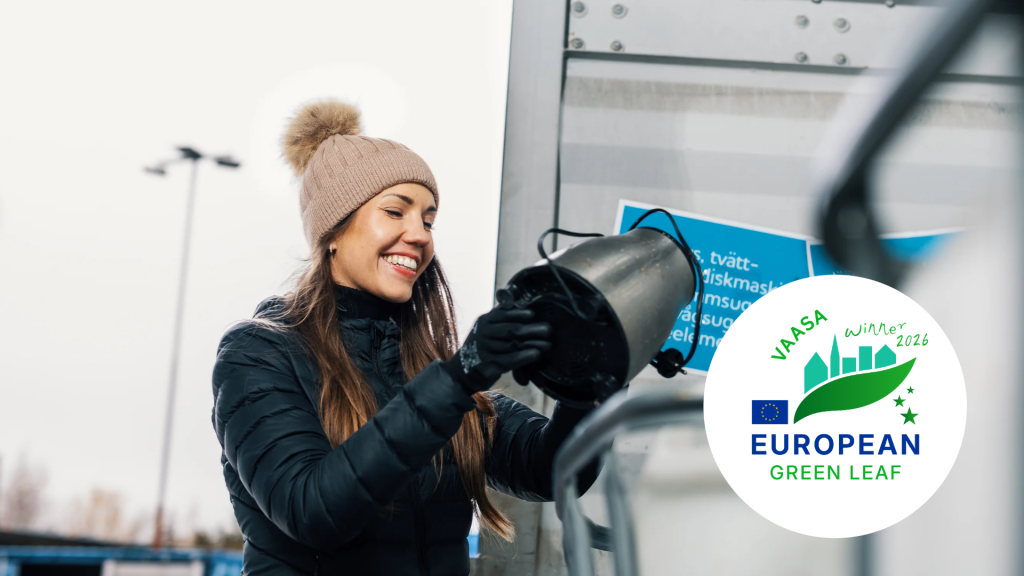 Nainen talvitakissa kaataa nestettä säiliöön jätehuoltopisteellä. Kuvassa näkyy Vaasa European Green Leaf 2026 -logo.