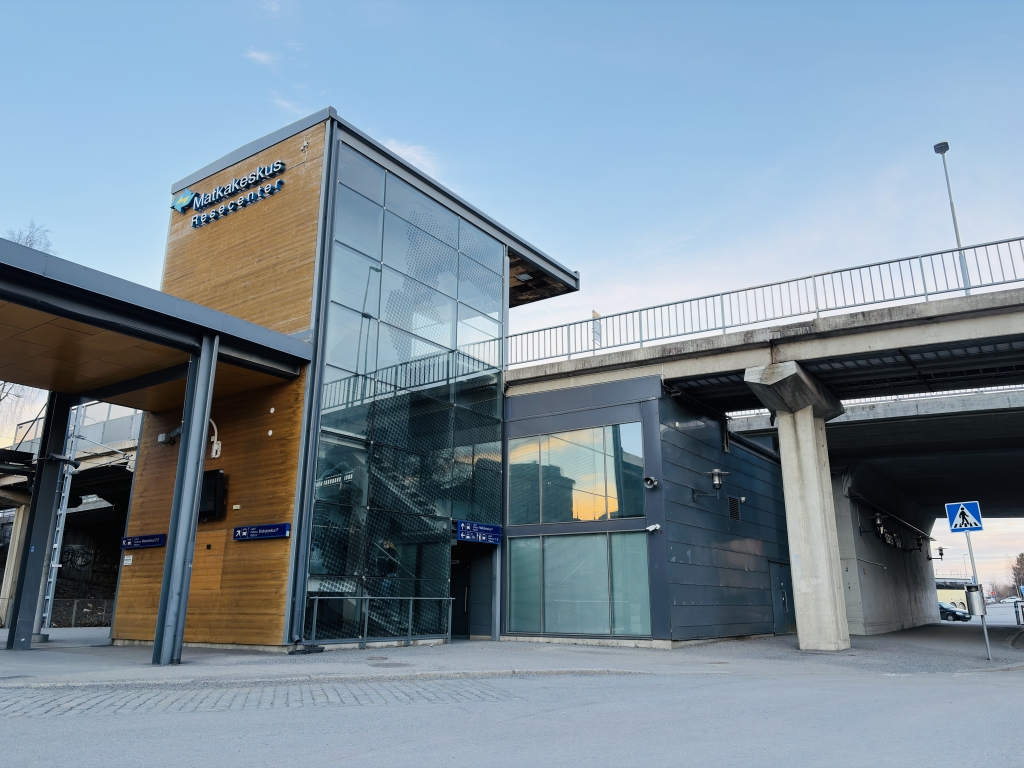 Rautatieaseman rakennus, jossa on lasiseinät ja puiset yksityiskohdat. Taustalla on ylikulkusilta.