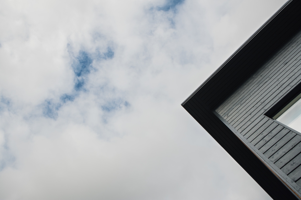 Det övre hörnet av ett nytt mörkgrått hus mot en molnig himmel.