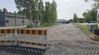 Keskeneräinen tietyömaa-alue, jossa näkyy liikenne-esteitä. Taustalla puita ja rakennuksia.