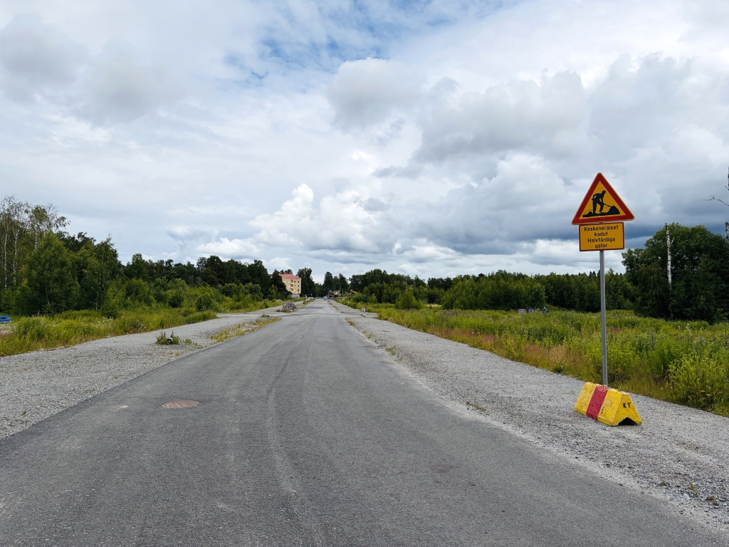 Asfalttitie, jossa on tietöistä varoitusmerkki tien vieressä. Taustalla on pilvinen taivas.
