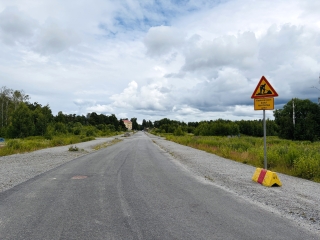 Asfalttitie, jossa on tietöistä varoitusmerkki tien vieressä. Taustalla on pilvinen taivas.