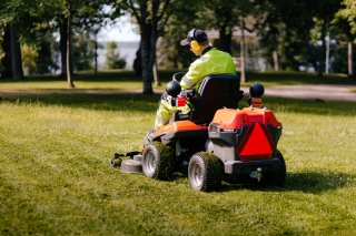 Henkilö ajaa ajoleikkurilla nurmikolla puistomaisemassa.