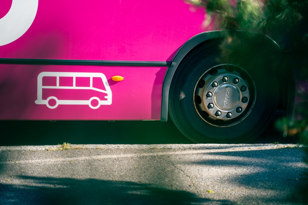 Lähikuva kirkkaan vaaleanpunaisen bussin renkaasta ja sivusta.