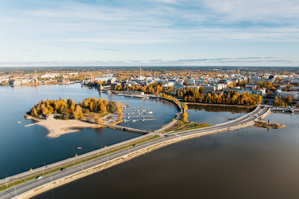 Ilmakuva kaupungista meren äärellä. Etualalla on pengertie ja pieni saari, taustalla kaupunki korkeine rakennuksineen. Taivas on sininen ja puissa syksyn värit.