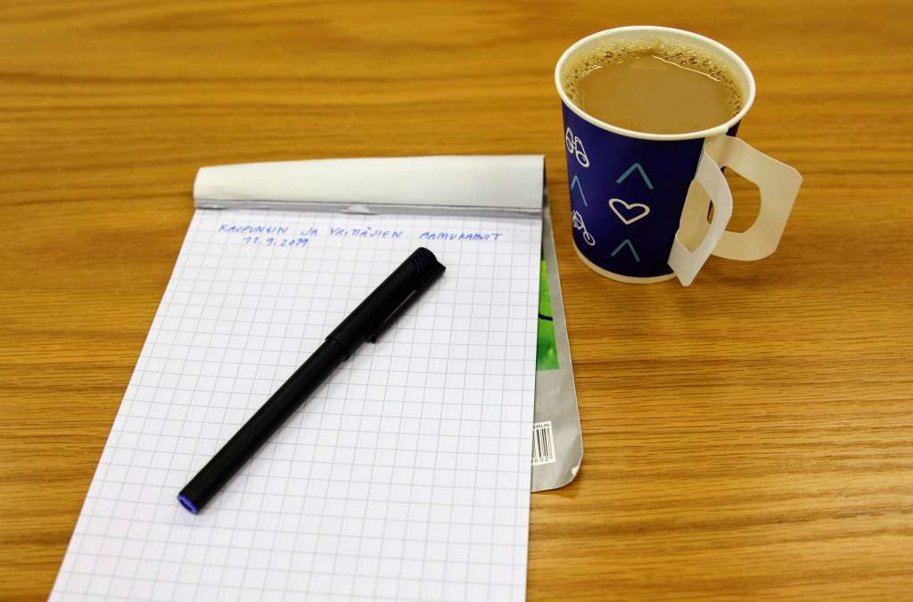 Kahvikuppi ja muistilehtiö pöydällä