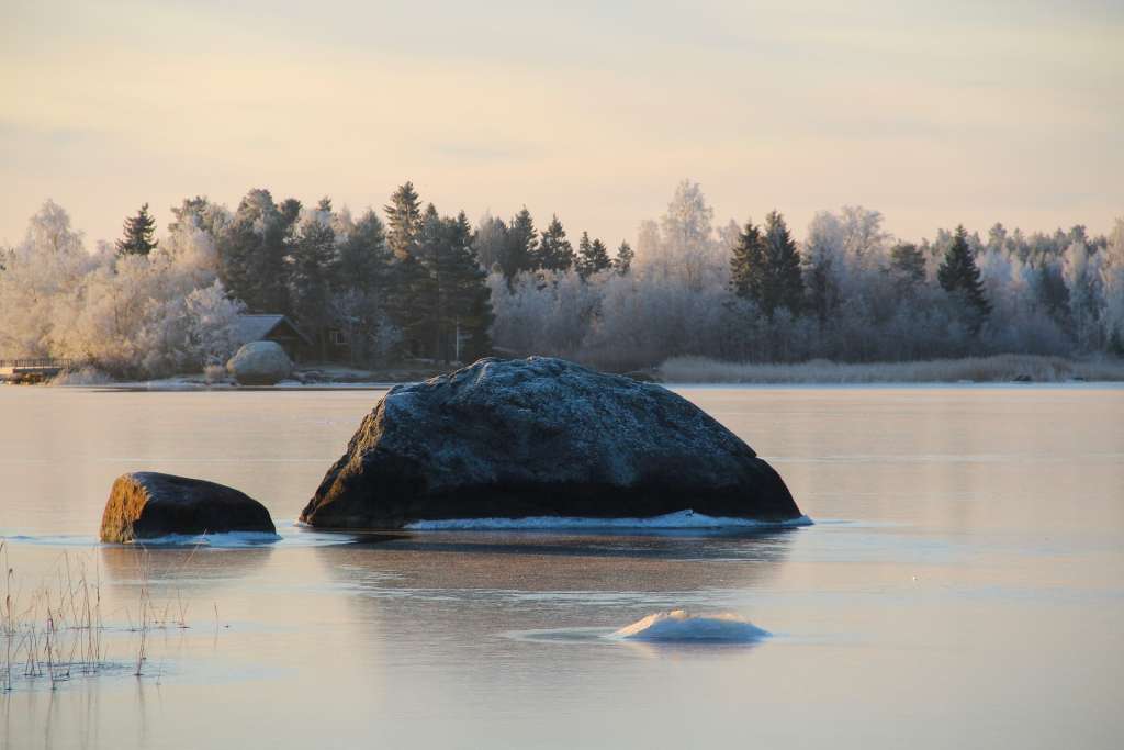 Suuri kivi jäätyneessä meressä, ja taustalla kuurainen metsä.