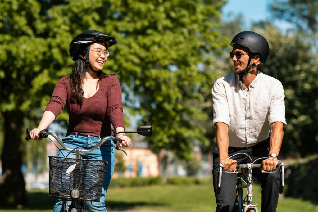 A woman and a man are riding a bike on a sunny day. There are green trees in the background.