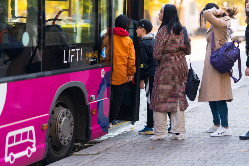 Lapsia ja naisia nousemassa vaaleanpunaiseen Lifti-bussiin