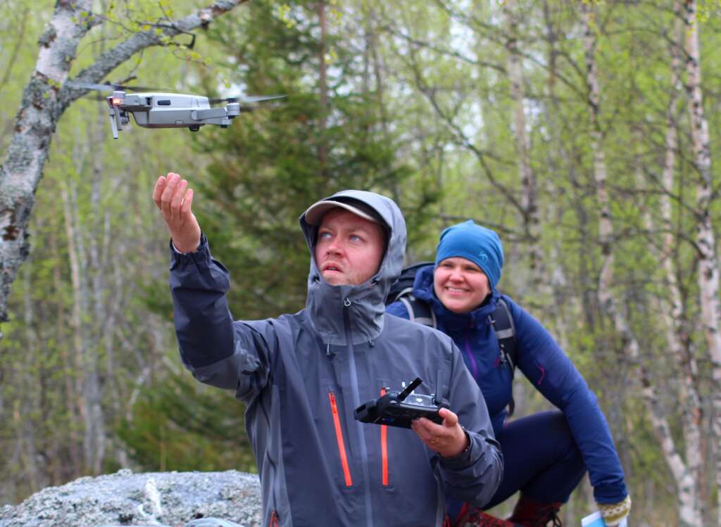 Kaksi henkilöä katselee, kuinka drone lähtee lentoon.