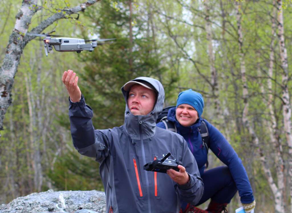 Two people watch as a drone is flying away.