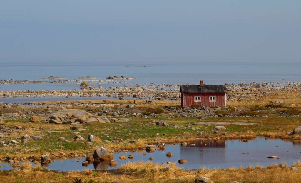 Punainen kalastajatupa kivisellä ulkosaarella, taustalla meri.