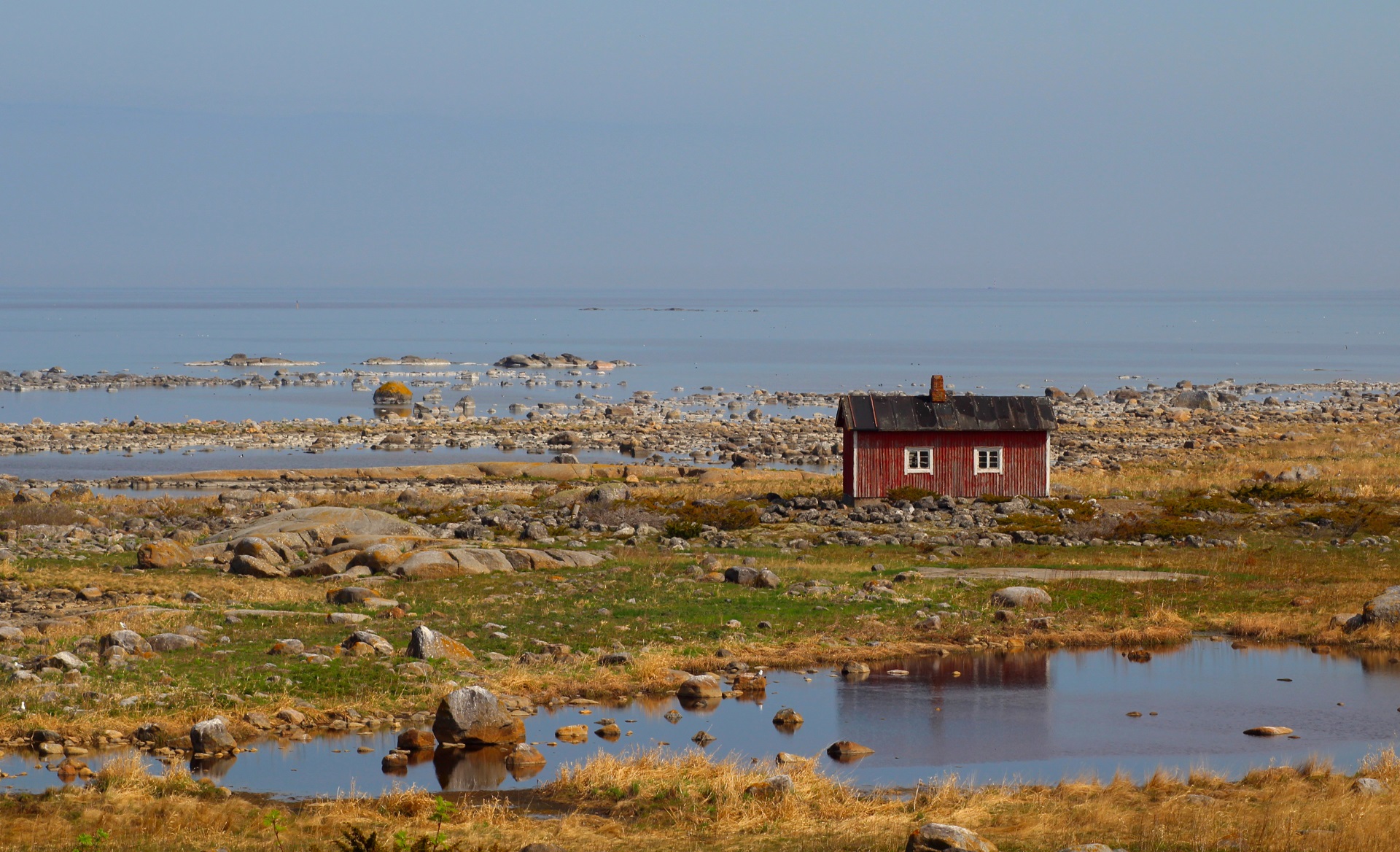 Punainen kalastajatupa kivisellä ulkosaarella, taustalla meri.