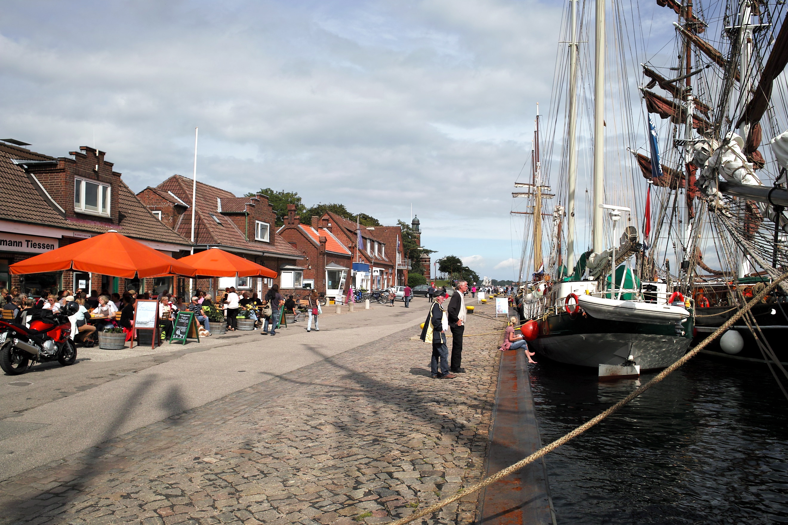 People walking at the dock and watching boats or sitting in a café.