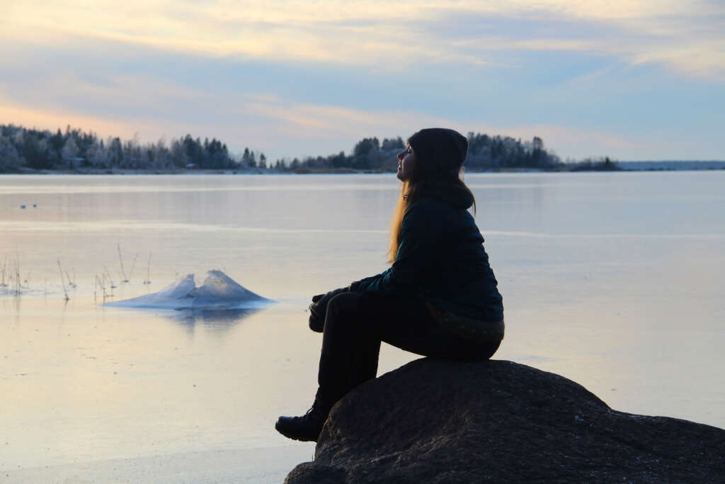 A person is sitting on a rock, which is arounded by frozen sea.