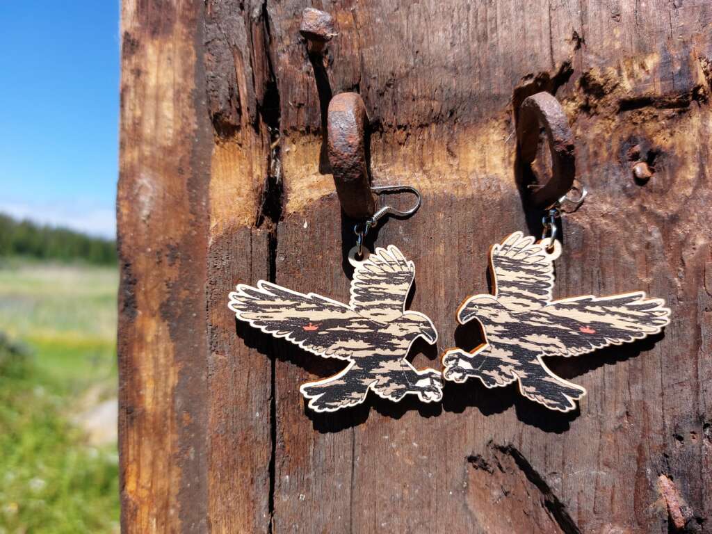 A pair of eagle earrings made of plywood and hanged against an old door.