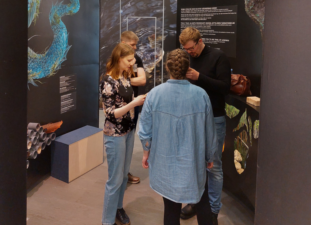 Four adults inspect something in a World Heritage exhibition.