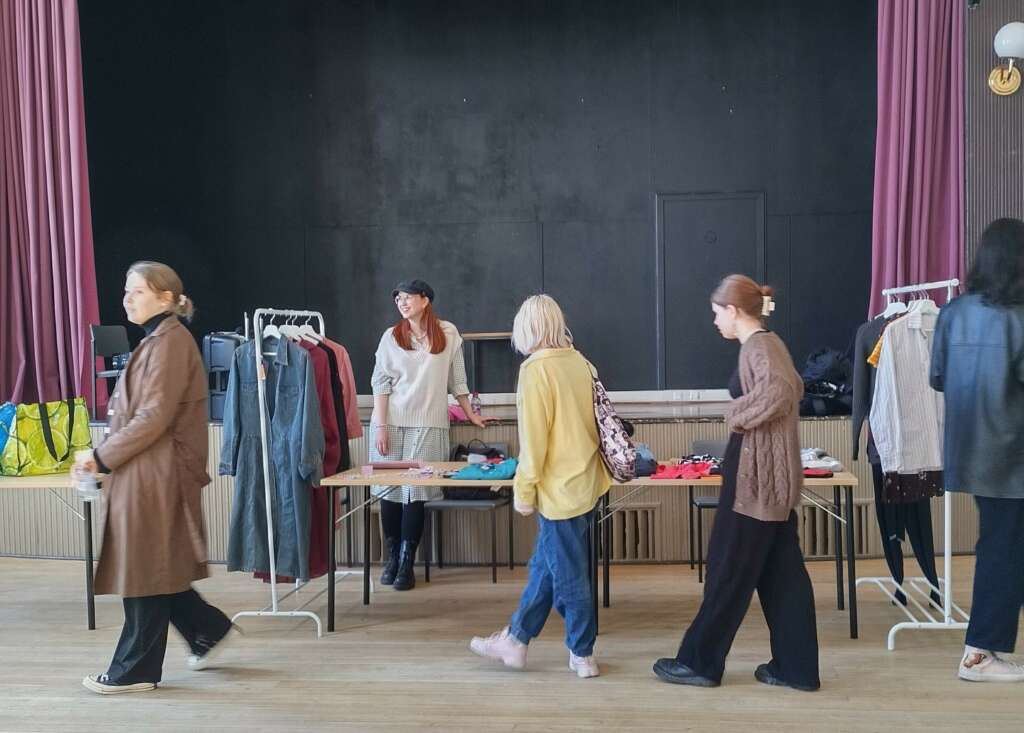 En kvinnlig studerande säljer begagnade kläder på kulturhuset Fanny, tre kvinnliga studerande är på väg förbi hennes stånd medan de tittar på produkterna.