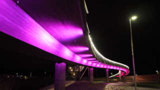 Cykelbron över Alskatvägen lyser lila i mörkret.