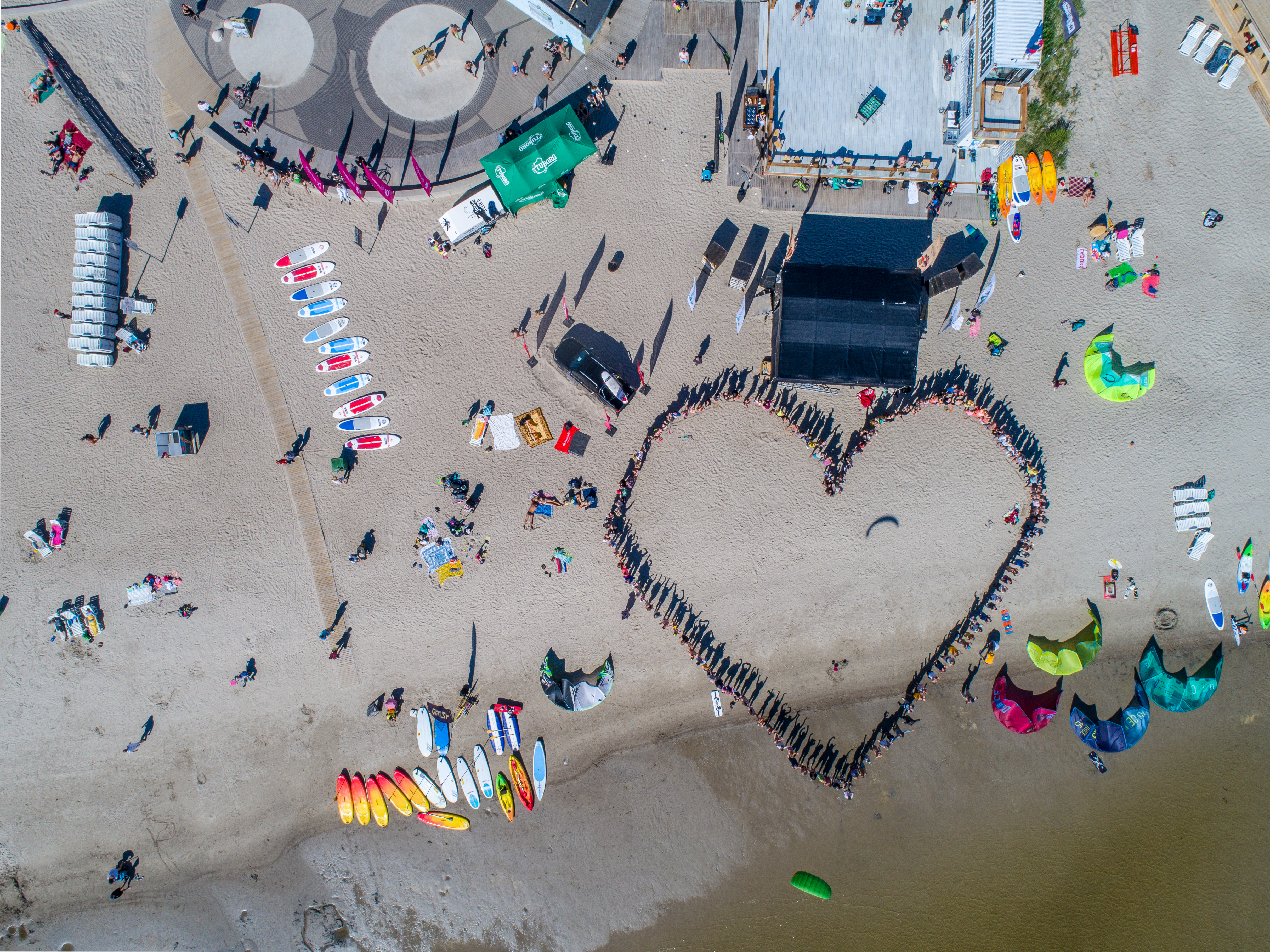 Beach with surfboards and people standing in the form of a heart.