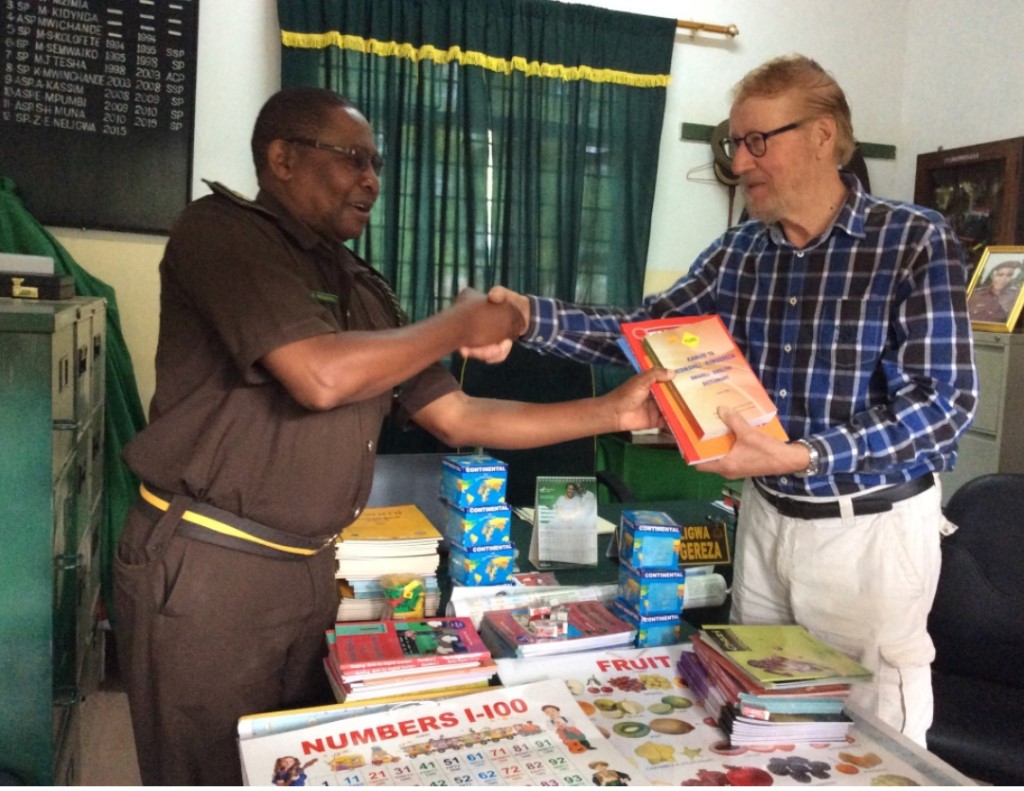 A man hands books and other material to another man as they shake hands.