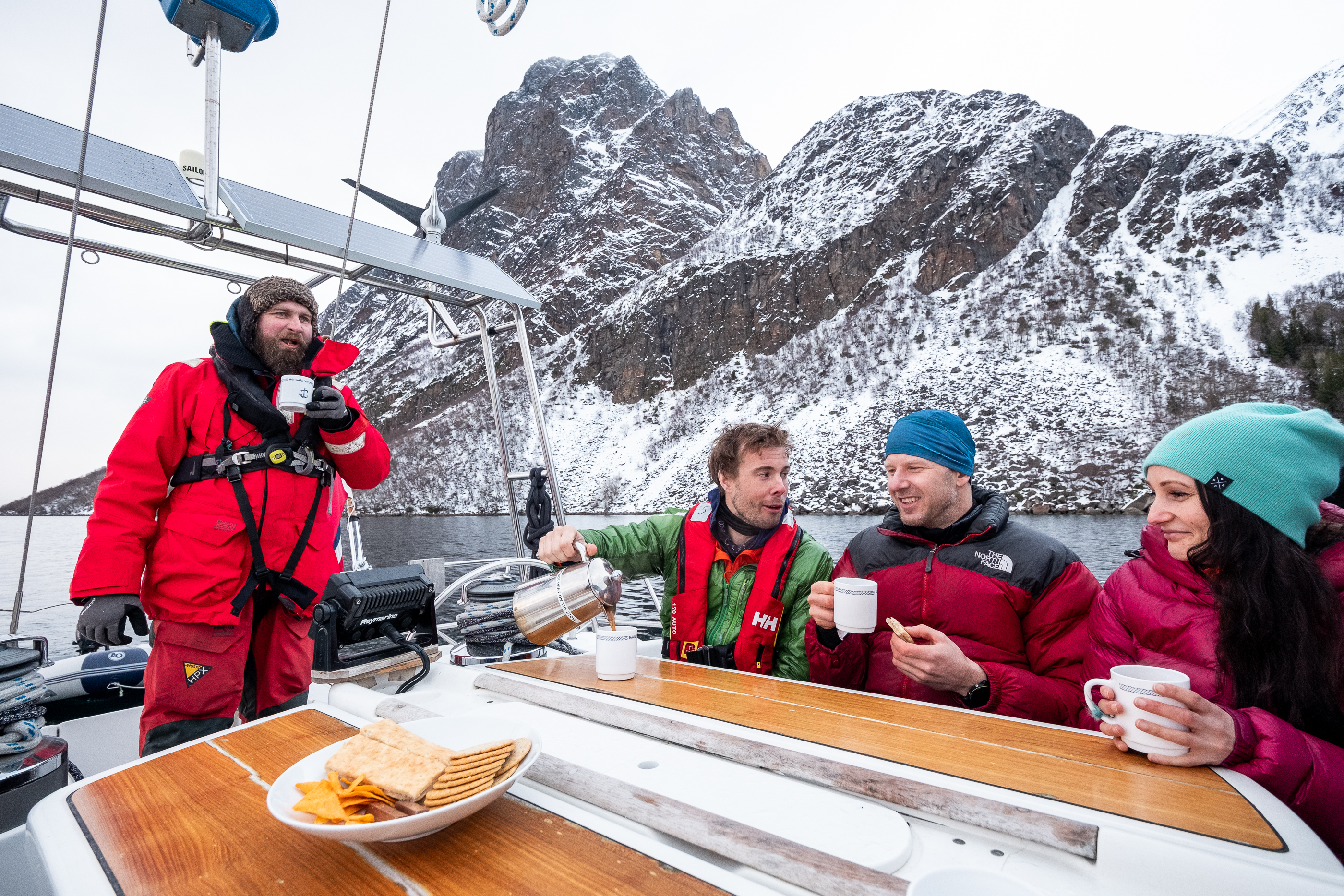 People drinking coffee on a sailing boat. Mountains in the background.